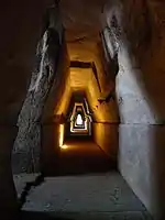 A dark stone corridor with light at the distant end