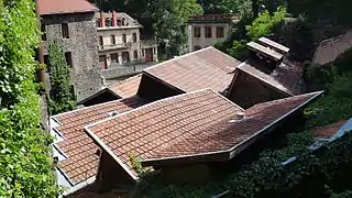 View of a group of mechanical tile roofs forming the buildings of the Forge Mondière and, in the background, 2 large industrial buildings.