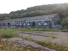 a long grey building, with concrete in the foreground and trees in the background