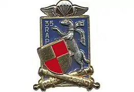 Blue Winged Rectangle with two crossed cannons reading Droit Devant topped by a red and gold shield armor