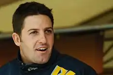 A man in his early twenties looking away from the camera and smiling widely