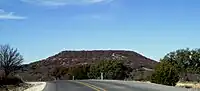 Round Mountain, a butte located 6&nbsp;mi (9.7&nbsp;km) to the northwest of Comanche, Texas, where Robert T. Hill first observed Lower Cretaceous fossils and strata. (31°55′30″N 98°42′07″W﻿ / ﻿31.925°N 98.702°W﻿ / 31.925; -98.702) (30 December 2008)