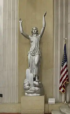 woman, nude above waist, raises both arms above head.