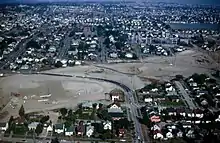 Aerial view of a suburban neighborhood with a diagonal swath cleared of homes and turned into dirt. A few roads cross over the dirt trench.