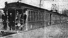 Electric railway cars, some with pantographs, at a wooden platform in an urban area