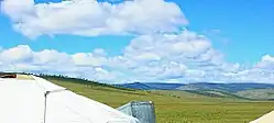 Puffy white clouds roll over lush green hills.