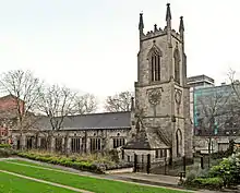 A substantial stone church seen from the north-west. The tower has crocketted pinnacles, and the north wall of the body of the church has a series of large rectangular windows